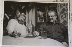 Two men at table with bottle and glasses