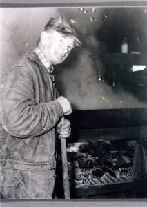 Factory worker stoking coal furnace with shovel