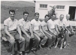 Seven men seated on bench with German shepherd