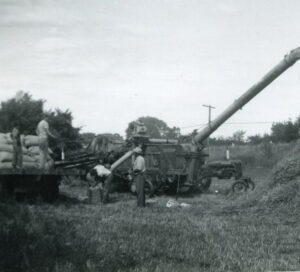 Men unloading grain with vintage farm auger