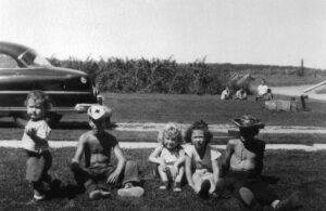 Five children sitting on grass beside vintage car