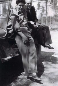 Two men in vintage attire leaning on car