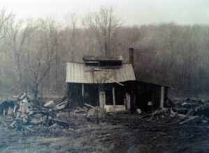 Abandoned weathered cabin amid debris and bare trees