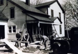 Three men repairing a wooden farmhouse exterior
