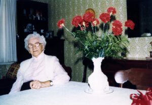 Elderly woman seated beside vase of red carnations